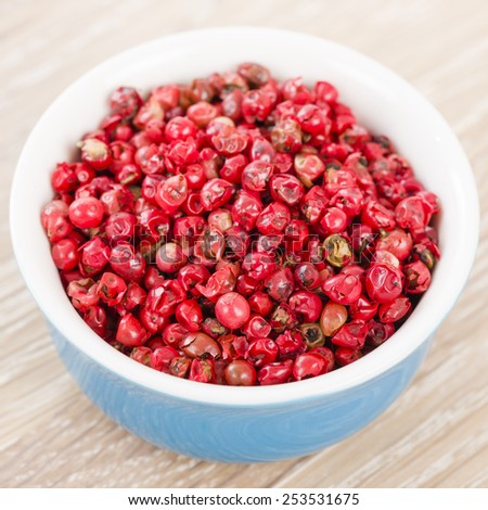 Pink Peppercorns - Bowl with dried pink peppercorns on a wooden background.