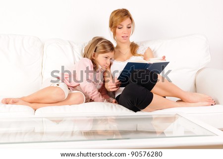 Mother reading a book with her daughter on white sofa
