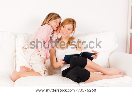 Mother reading a book with her daughter whispering in her ear