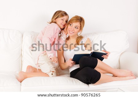 Mother reading a book with her daughter whispering in her ear