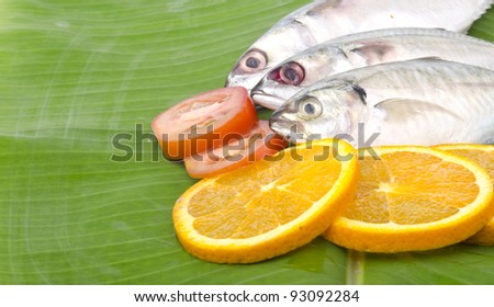 Fresh fish, spices and lemon at side of frame with banana leaf as background.