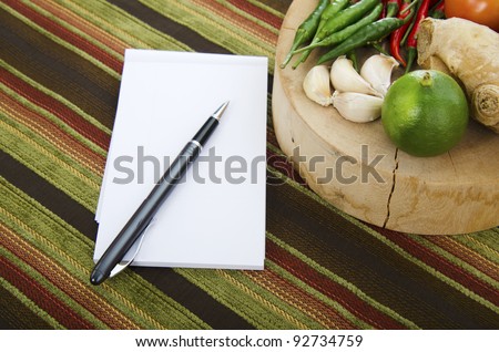 A cooking ingredients on wood plate with notebook and pen on side with lining texture as background.