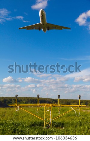 white jet passenger aircraft with the gear against the blue sky and landing lights and green grass