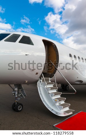 white private jet and open ladder, red carpet at the airport on a background blue sky