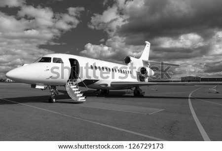 White reactive private jet, the front landing gear and a ladder on blue sky and clouds