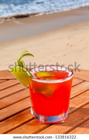 red alcohol cocktail on wooden table with crushed ice on background blue sky and sea