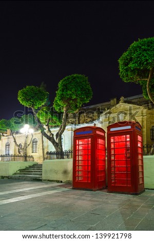 red English telephone box on Malta a summer night in the light of lanterns with trees