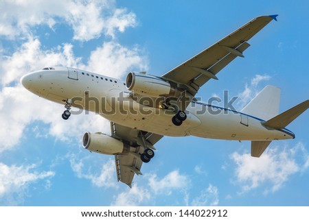 view from below on the white jet passenger aircraft with the gear against the blue sky