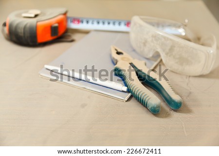 pliers, notebook, tape measure and safety glasses under a layer of dust on the table