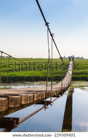 Pedestrian suspension bridge of steel and wood over the river, summer in Russia