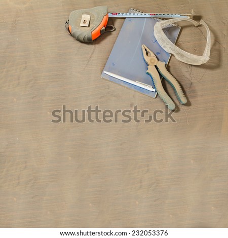 pliers, notebook, tape measure and safety glasses under a layer of dust on the table