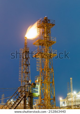 burning torch and industrial tower of metal on a chemical plant at night
