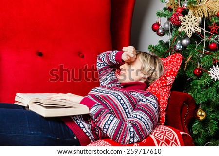 young woman fell asleep with a book on a red couch at Christmas tree