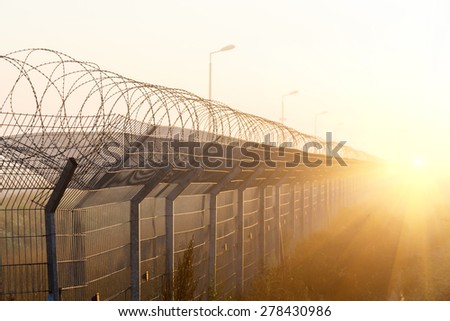 fence with barbed wire on the border of the object at dawn with fog in the summer, russia