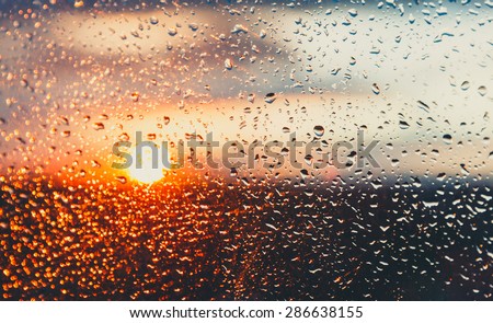 Water drops on a window glass after the rain. The sky with clouds and sun on background.