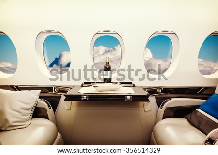 Luxury interior in bright colors of genuine leather in the business jet, sky and clouds through the porthole