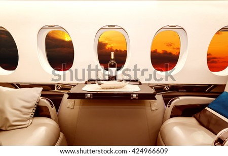 Luxury interior in bright colors of genuine leather in the business jet, sky, clouds and sunset through the porthole