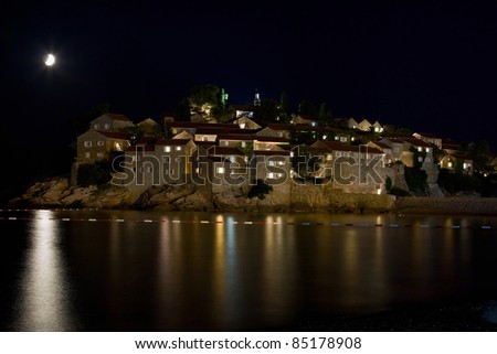 reflection of the moon and the lights in the water of the Adriatic Sea on the background of the walls of the old houses of Sveti Stefan