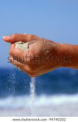 female hand with falling out of it with sand on a background of blue sky and sea in summer
