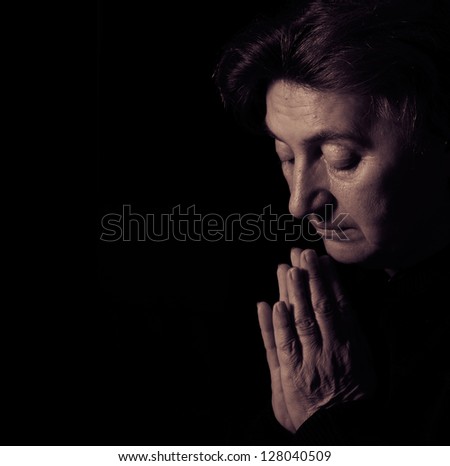 Senior female prayer. Low-key studio lighting.