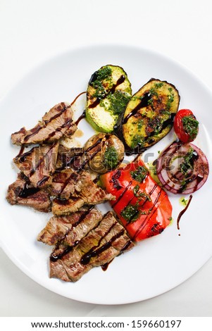 Grilled flank beef steak with grilled vegetable on white plate. Overhead shot