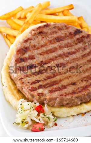 Traditional serbian burger patty  served with some fresh fries and visible grill marks on a homemade pita bred