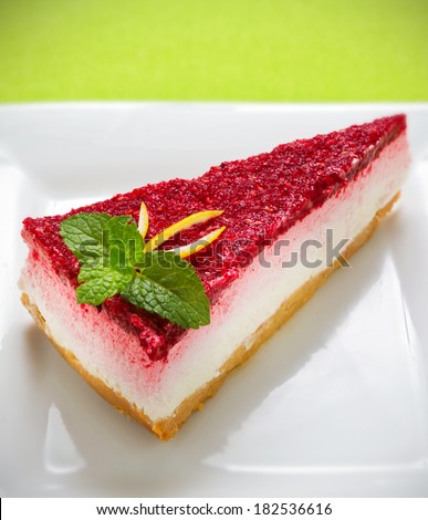 The typical Cheesecake rich and dense, smooth, and creamy consistency with raspberry sauce on green background