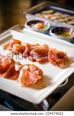 Prosciutto cold cuts served on plate as a part of stylish banquet table
