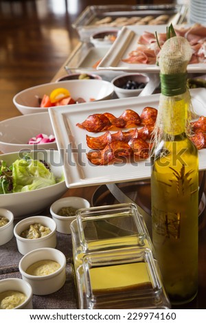 Detail from large hotel breakfast buffet table with olive oil, cold cuts and some vegs