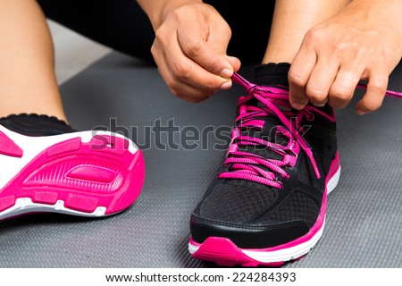 Woman tying her sports shoes on exercising mat