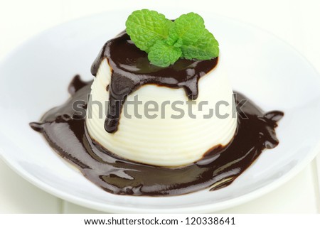 Italian dessert panna cotta served on a white plate with chocolate sauce and fresh mint