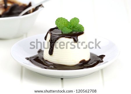 Italian dessert panna cotta served on a white plate with chocolate sauce and fresh mint