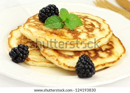 Delicious breakfast - fluffy pancakes topped with honey, fresh blackberries and a sprig of aromatic mint