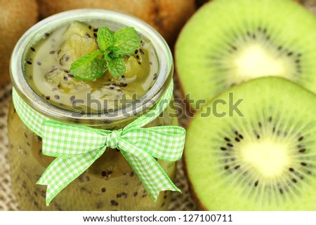 Delicious homemade kiwi jam in a glass jar with a decorative bow and fresh kiwi fruit and mint sprigs