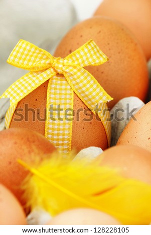 One Easter egg decorated with a yellow bow among other non decorated eggs in the carton packaging
