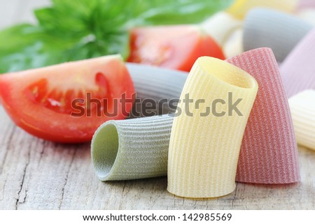 Italian cuisine concept - tri coloured pasta representing Italian flag with sliced tomatoes and fresh basil at the background