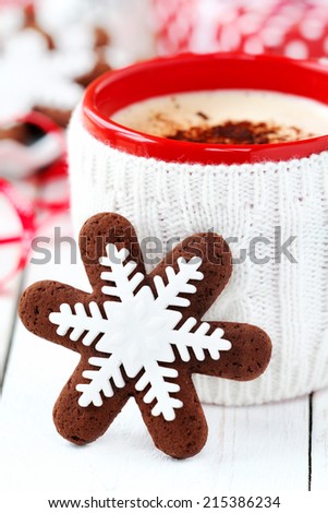 Snowflake decorated chocolate Christmas cookie with a red mug of cappuccino dressed in knitted mug holder