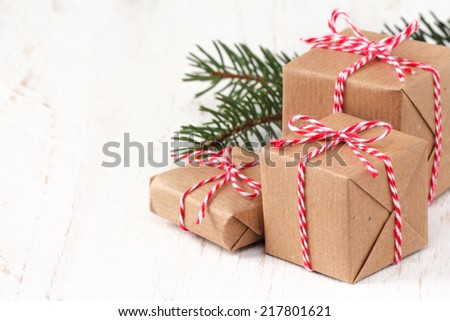 Group of three Christmas presents wrapped in brown paper and ties with a festive red and and white baker\'s twine on white wooden background with copy space