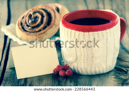 Cozy rustic Christmas setting - red mug of black coffee  in a white knitted cup holder with a wrapped gift and a greeting card with retro vintage filter effect