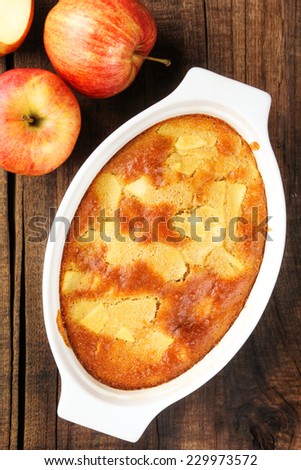 Homemade Charlotte pie made of Gala apples in oval baking bowl on a rustic wooden kitchen table. Overhead view