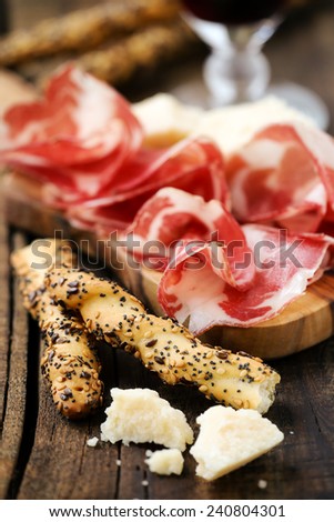 Traditional Italian appetizer - Rustic breadsticks with poppy, sesame and flax seeds, pieces of parmesan and thin slices of coppa or capicola ham