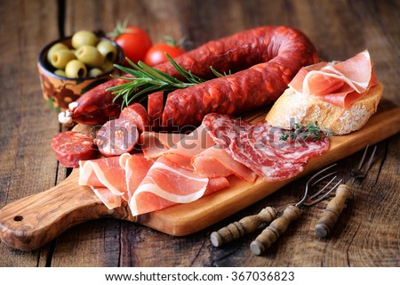 Cured meat platter of traditional Spanish tapas - chorizo, salsichon, jamon serrano, lomo - erved on wooden board with olives and bread