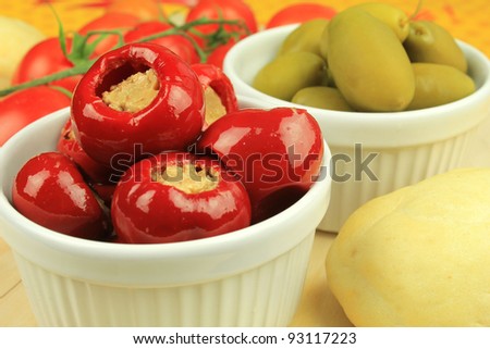 Red cherry pepper, or pimento, stuffed with tuna with green olives and tomatoes at the background
