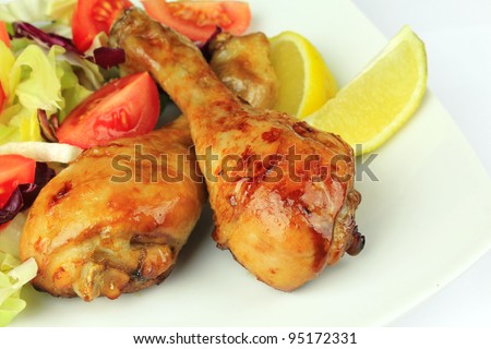 Homemade roasted chicken drumsticks served on a white plate with lemon and salad