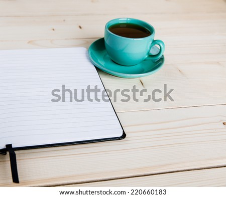 Open a blank white notebook, pen and cup of tea on the desk