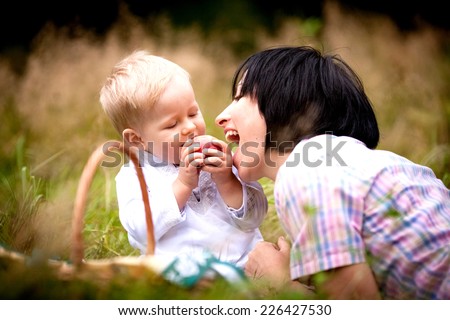 Little boy feeds mum apple. Family on picnic in the forest. Happy family on a summer outing