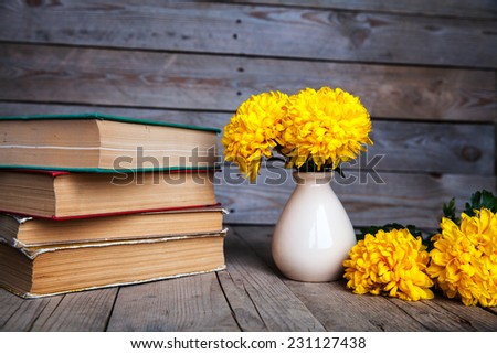 Beautiful yellow chrysanthemum on the old wooden background. Vintage books. Pottery vase with flowers.