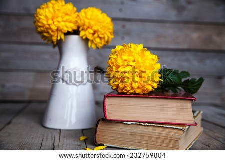 Flowers. Beautiful yellow chrysanthemum in a vintage vase. Old books on a wooden background.