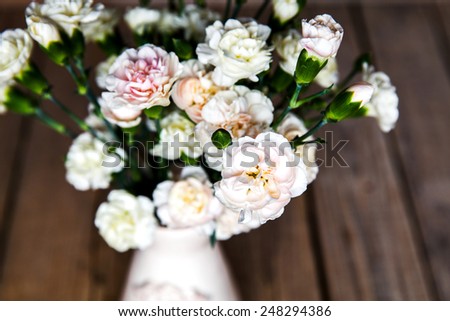 delicate bouquet of carnations in a vase on a vintage wooden background