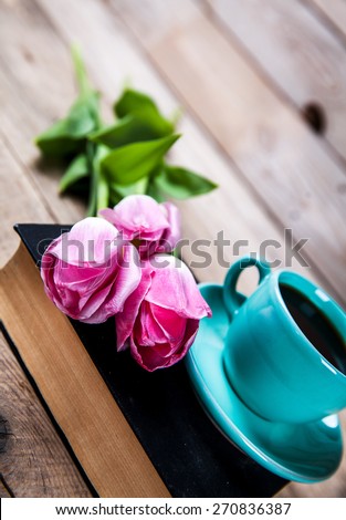 Cup of hot coffee on book with flowers on table on dark background